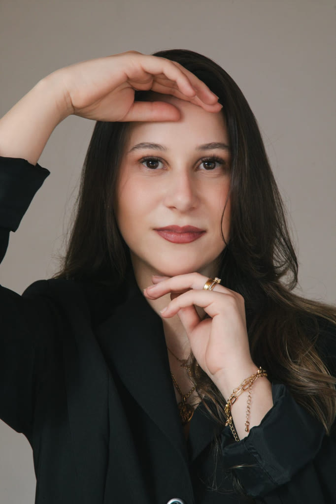 Dra. Júlia de blazer preto com as mãos emoldurando o rosto